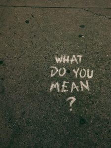 The words "What do you mean?" written in chalk block-letters on pavement