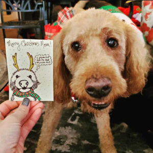 a photo of a dog who is illustrated on a hand-drawn Christmas card held in a person's hand