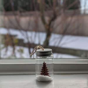a christmas ornament of a tree cut-out in a small glass jar set on a windowsill