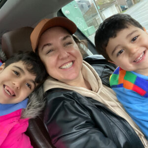 a woman and two children smile at the camera from the seat of a car