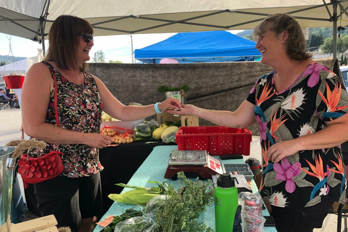 two women reach toward each other over a table full of produce