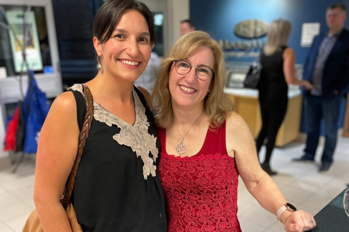 two women stand nex to each other and smile at the camera