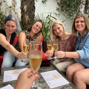 four women hold glasses of wine and smile at the camera