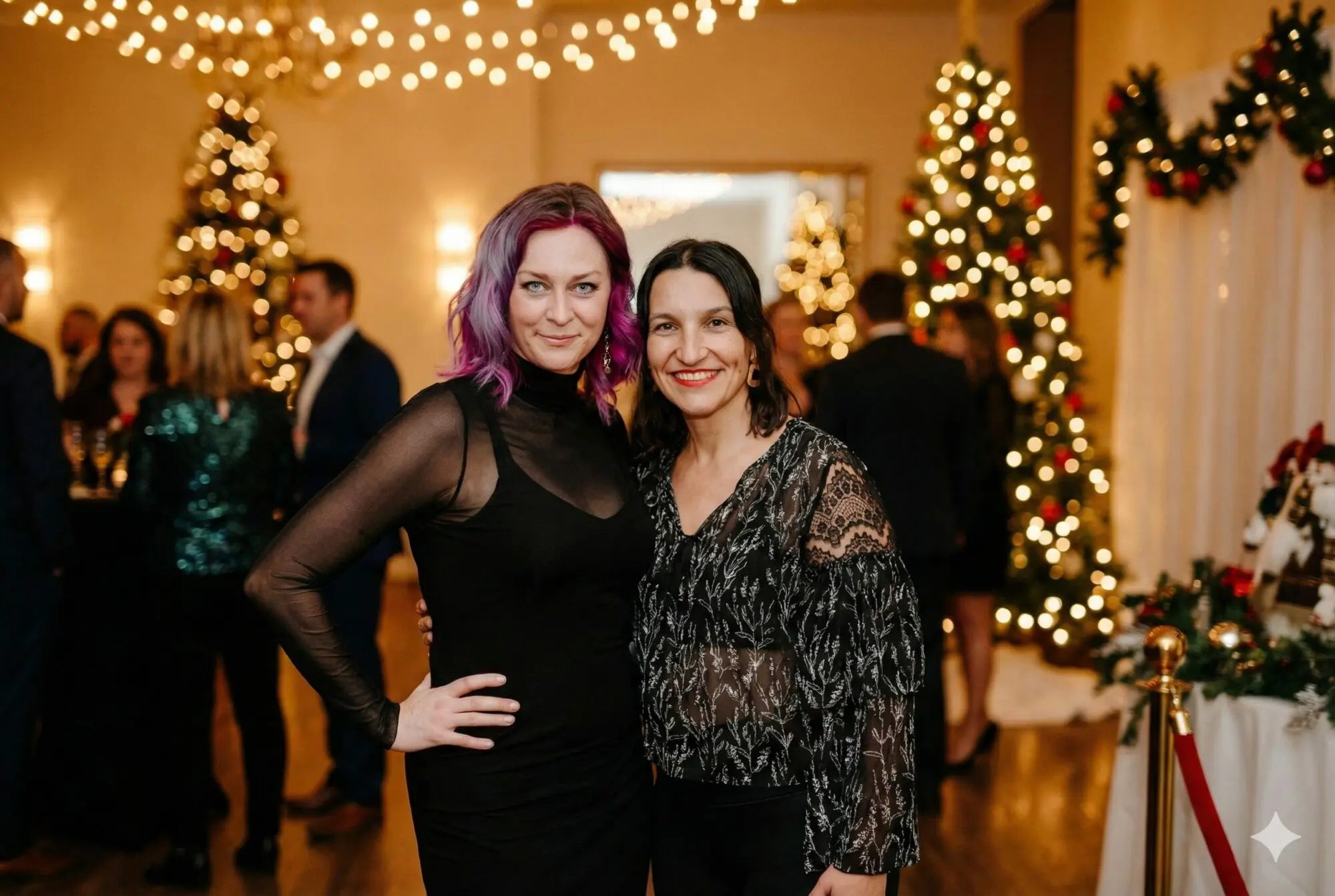 Two women (Kyla and Val) stand together facing the camera smiling in a holiday party setting